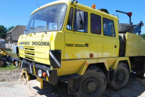 Żółta ciężarówka zaparkowana na polnej drodze w galerii zdjęć.